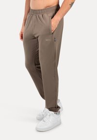 Herren braune Sporthosen aus leichtem Material, mit elastischem Bund, Seitentaschen und einem kleinen Logo-Detail.