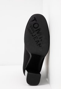 Černý vysoký podpatek s texturovanou látkou a pevným gumovým podešvem. Na spodní straně je vyražené logo "TOMMY JEANS".