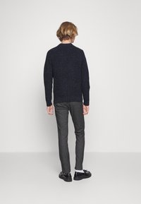 Pull en maille bleu marine avec un motif texturé, col rond, et pantalon gris ajusté. Chaussures noires à finition texturée.