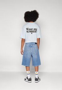 Lyseblå cropped t-shirt med sort tekst "Vil du have mit NUMMER?" på bagsiden, parret med lyseblå denim shorts og sorte sneakers.