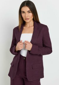 Lila linneblazer med en skräddarsydd design, slagfickor, två framfickor och enkel knäppning, bärs över en vit topp.