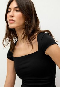 Schwarz kurzärmliges Oberteil mit quadratischem Ausschnitt, aus glattem Stoff gefertigt. Verfügt über eine figurbetonte Passform und einen minimalistischen Look.