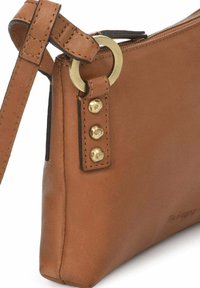 Sac à main en cuir marron avec fermeture éclair, doté d'une ring en métal doré et de trois clous en laiton sur la sangle. Texture lisse et design élégant.