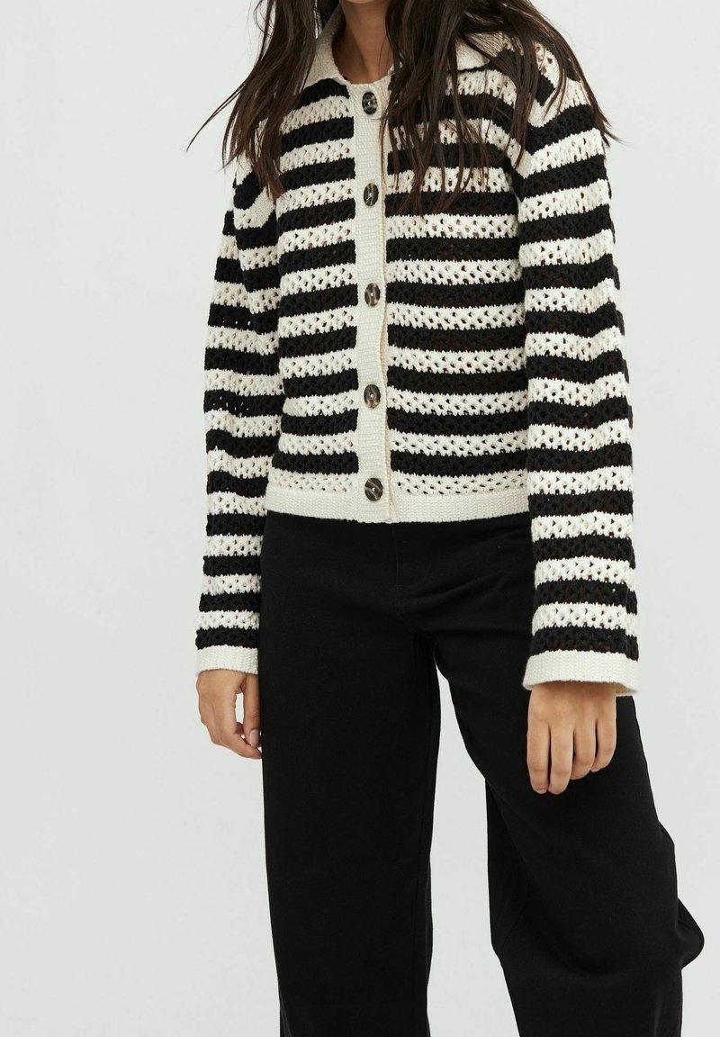 Cardigan tricoté à rayures noires et blanches avec un devant boutonné et des poignets côtelés. Il présente un col uni contrastant et des boutons détaillés.