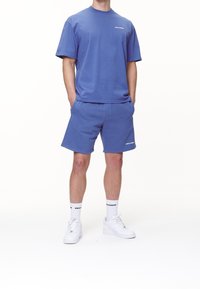 T-shirt bleu clair à manches courtes et short assorti en coton, arborant un logo de marque. L'ensemble est complété par des baskets blanches et des chaussettes.