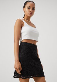 Crop top i hvit bomull, kombinert med et sort blondeskjørt med blomsterdesign og en bølget kant. Glatt tekstur og tettsittende fasong.