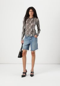 Haut à manches longues à imprimé serpent dans des couleurs atténuées, associé à un short en denim bleu clair avec des bords effilochés. Chaussures à talons noires et sac à main.
