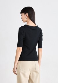 Svart kortermet topp med vid halsudskæring. Glat stof, tætsiddende design, parret med lysebeige højtaljede bukser med baglommer.