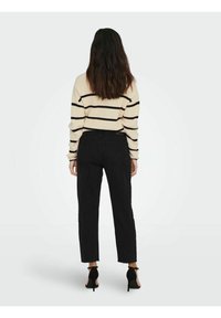 Zwarte hoge taille broek met een recht gesneden pijp, gecombineerd met een crèmekleurige trui met horizontale zwarte strepen. Gestreepte gebreide structuur.