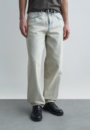 Világos mosású, bő szabású farmer látható varrással, ötpocketes kialakítással és fekete övvel. Fekete, lapos, bebújós cipővel párosítva.
