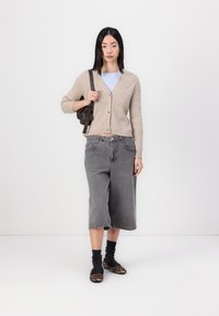 Beige ribbed cardigan, gray wide-leg denim culottes, black socks, and leopard print flats. Model holds a dark bag. Plain background.