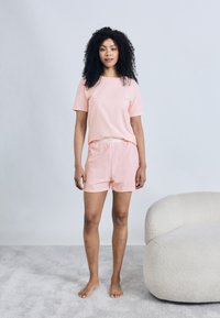 Σετ άνετης βαμβακερής ενδυμασίας απαλό ροζ χρώμα, με κοντομάνικη μπλούζα και σορτς, μαλακή υφή και ελαστική μέση, συνδυασμένο με γυμνά πόδια.