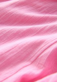 Weicher, strukturierter Stoff in einem lebhaften hellrosa Farbton, mit dezenten Falten, die ein wellenförmiges Muster über die Oberfläche erzeugen.