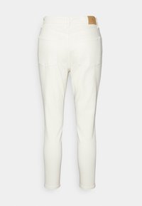 Bílé denimové kalhoty s přiléhavým střihem, které mají dvě zadní kapsy a koženou značku v barvě tan na pase. Hladká textura a čistý design.