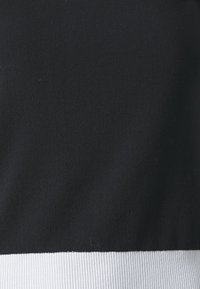 Haut noir avec un ourlet côtelé blanc, fabriqué dans un tissu doux. Le design présente une texture lisse et une transition nette entre les couleurs.