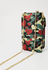 Multicolored camouflage-patterned bag featuring red hearts, textured faux leather, gold chain strap, and a zip closure.