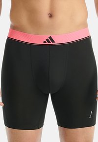 Mannelijk bovenlichaam in zwarte sport compressieshort met een roze tailleband en het Adidas-logo aan de voorkant in het midden.