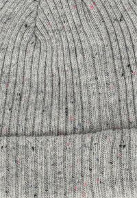 Grauer Strickbeanie mit gerippter Textur, durchzogen von bunten Flicken in Pink, Blau und Schwarz im Stoff.