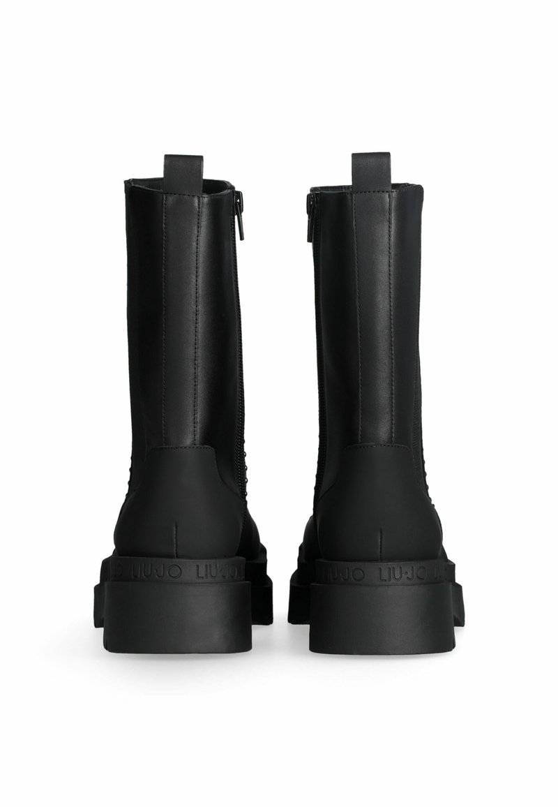 Bottines en cuir noir avec une semelle en caoutchouc épaisse, dotées d'une fermeture éclair et d'un panneau arrière texturé. L'étiquette de la marque est embossée sur le talon.