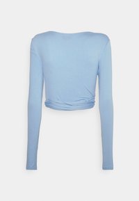 Ljusblå långärmad topp med rundad halsringning och en knuten detalj vid midjan, tillverkad av ett slätt, stretchigt tyg.