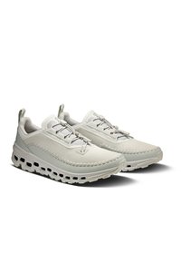 Light gray athletic shoes featuring a textured upper, rounded toe, decorative stitching, and a chunky sole with ventilation cutouts.