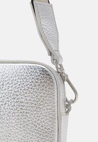 Borsa a tracolla argentata con texture, dotata di una morbida tracolla in pelle e una chiusura a clip metallica. Presenta una forma rettangolare con cuciture dettagliate.