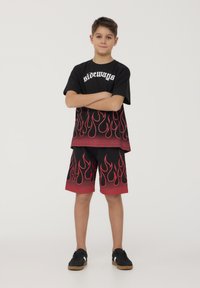 Maglietta nera con testo bianco "sideways" e motivo di fiamme rosse. Pantaloni corti neri coordinati con la parte superiore, con fiamme rosse all'orlo. Sneakers nere.