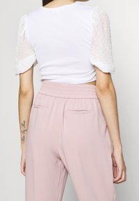 Bílý ribbed crop top s průhlednými nabíranými rukávy s texturovanými tečkami, v kombinaci s růžovými kalhotami s vysokým pasem, elastickým pasem a kapsami.