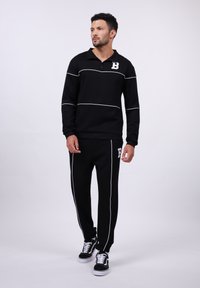 Black athletic set with a quarter-zip jacket featuring white piping and a logo, paired with tapered pants, also accented with white lines.