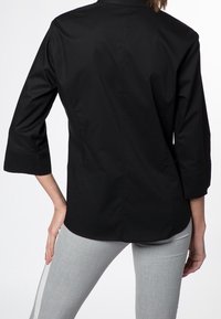Chemise noire à manches longues avec un col classique, présentant une texture lisse et une coupe ajustée, vue de dos.