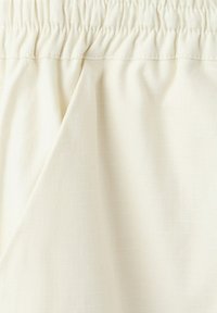 Material crem cu talie elastică adunată și detaliu cu buzunar pe cusătura laterală pe pantaloni sau pantaloni scurți ușori.