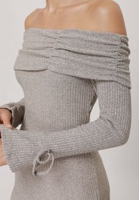 Grijs geribbelde off-shoulder jurk met lange mouwen en geplooide details. Bevat een strikaccent aan de uiteinden van de mouwen. Zachte, gestructureerde stof.