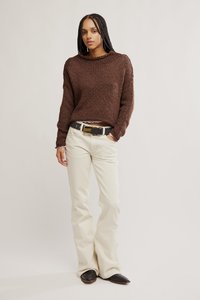 Καφέ πλεκτό πουλόβερ με στρογγυλή λαιμόκοψη, συνδυασμένο με κρεμ παντελόνι καμπάνα και μαύρη ζώνη. Μαύρα παπούτσια με μυτερό νύχι ολοκληρώνουν το σύνολο.