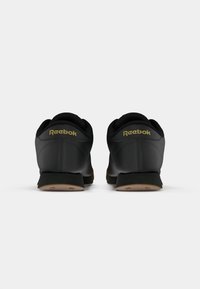 Sapatos Reebok pretos com um cabedal liso, colarinho acolchoado e logo dourado subtil. Sola em borracha de goma e design de bico arredondado.