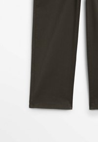 Gros plan sur le bas des jambes d’un pantalon vert olive foncé à ourlets droits, sur fond blanc uni.