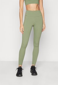 Olive green high-waisted leggings made from stretchy material, featuring a smooth texture and fitted design. Paired with black athletic shoes.