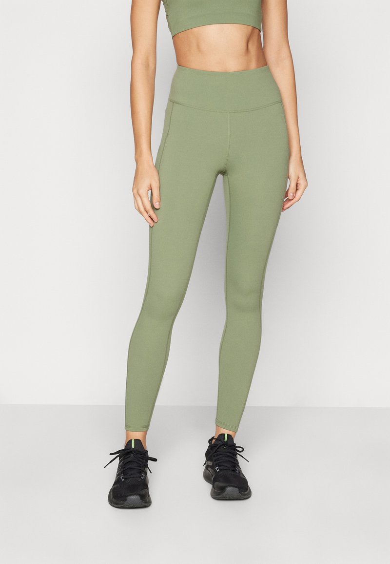 Olive green high-waisted leggings made from stretchy material, featuring a smooth texture and fitted design. Paired with black athletic shoes.