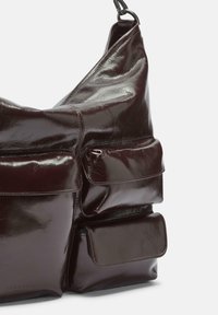 Dunkelbraune, glänzende Leder-Schultertasche mit drei vorderen Klappentaschen und verstellbarem Riemen, der oben sichtbar ist.