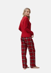 Top rojo de manga larga combinado con pantalones de cuadros en rojo, negro y blanco. Tejido suave, corte relajado y costuras visibles. Sin herrajes visibles.