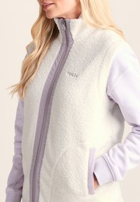 White fleece vest with lavender accents, featuring a high collar, front zipper, and side pockets. Soft texture and stylish design.