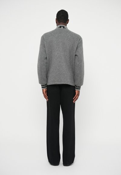 Γκρι πουλόβερ από μάλλινο ύφασμα με ψηλό γιακά και μαύρες λεπτομέρειες, συνδυασμένο με μαύρα παντελόνια ευρείας γραμμής. Διαθέτει χαλαρή εφαρμογή και υφαντό ύφασμα.