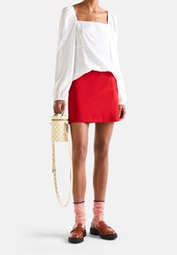 Biała bluzka z bufiastymi rękawami, czerwona mini spódnica, brązowe mokasyny, różowe skarpetki w prążki, żółto-biała torebka w kratę z paskiem.