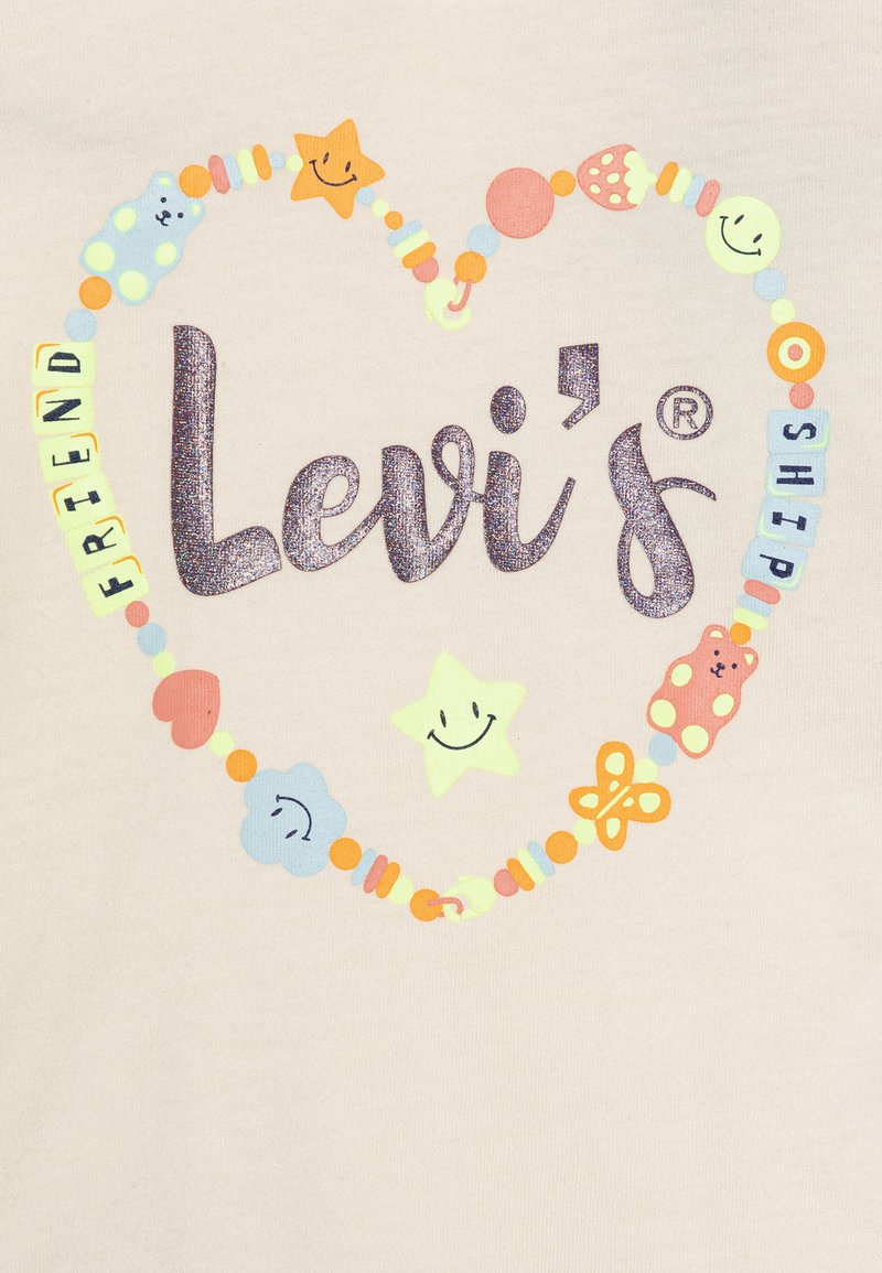 Crème-kleurige stof met een hartontwerp van multikleurige kralen en speelse iconen, met "Levi's" gedrukt in sprankelende donkere letters.