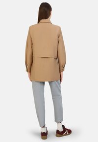 Brown jacket with a relaxed fit, featuring a collar and gathered sleeves, paired with light gray jeans and burgundy sneakers.