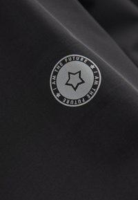 Black fabric featuring a circular logo with a star and the text “I AM THE FUTURE” in contrasting colors. Smooth texture, subtle grid pattern.