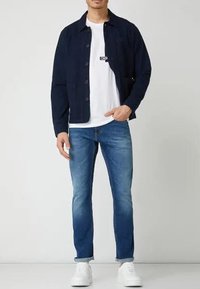 Navy button-up jacket over a white t-shirt, paired with light blue jeans and white sneakers. Casual, fitted design with visible stitching.