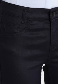 Dark blue denim jeans featuring a slim fit, front pockets, and subtle stitching details. Smooth texture with a slight sheen.
