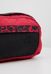 Sac North Face noir et rouge avec un motif abstrait rouge et noir sur le panneau supérieur et un logo embossé sur la poche avant noire.