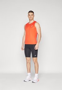 Top atlético naranja sin mangas, pantalones cortos ajustados negros y zapatillas blancas con acentos naranjas. Tela suave con un logo en el top.