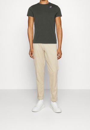 Camiseta de algodón verde con cuello redondo y mangas cortas, combinada con pantalones beiges y zapatillas blancas. Diseño minimalista, sin patrones.